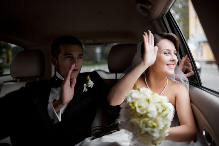 Newlyweds,Wave,With,Their,Hands,While,Sitting,In,The,Car